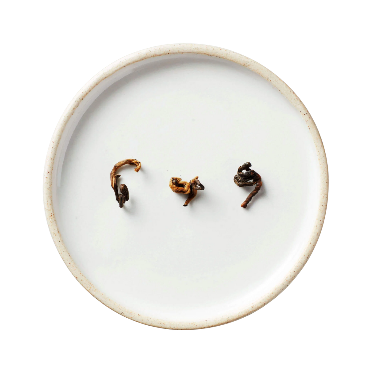 Hugo Grey | Black Blend tea leaves, dark brown with golden tips, rest on an off-white ceramic plate with a speckled rim, showcasing quality Yunnan tea.