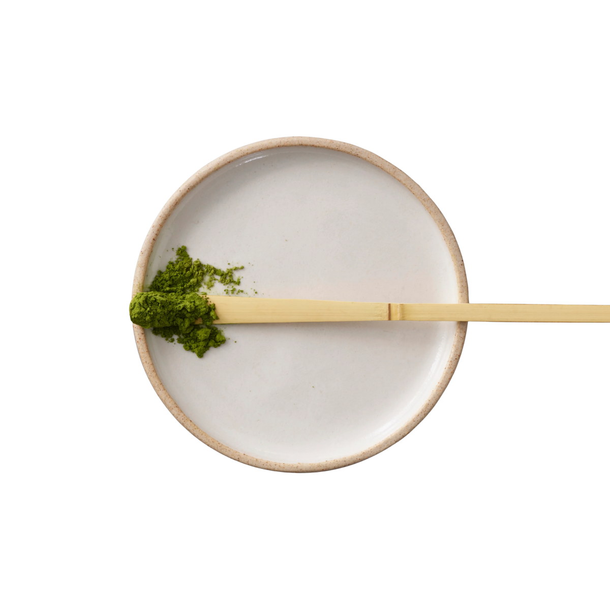 Ceramic bowl with green matcha powder and a wooden spoon on a white background