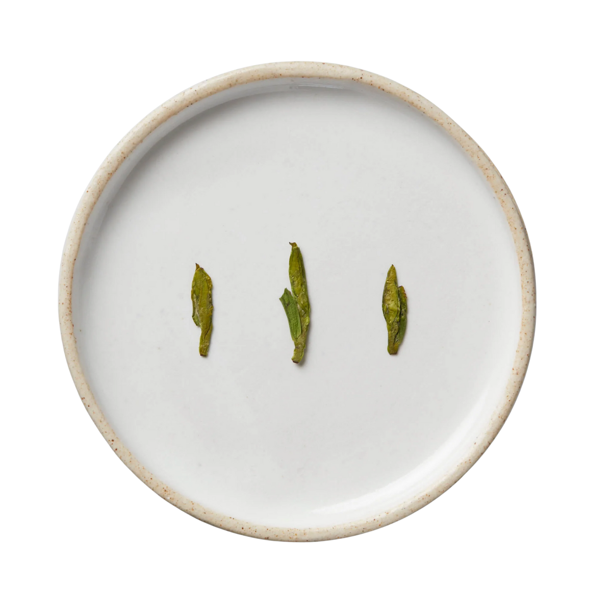 Session Longjing | Green: Top-down view of white-glazed ceramic plate displaying neatly lined dried Longjing tea leaves, showcasing its quality and craftsmanship from Xinchang, China.