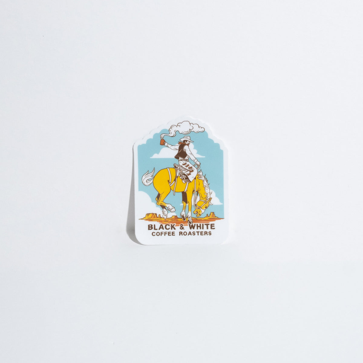 A die-cut sticker featuring a cowboy riding a yellow horse against a light blue sky, with the text 'BLACK & WHITE COFFEE ROASTERS' below the illustration, shown on a plain white background.