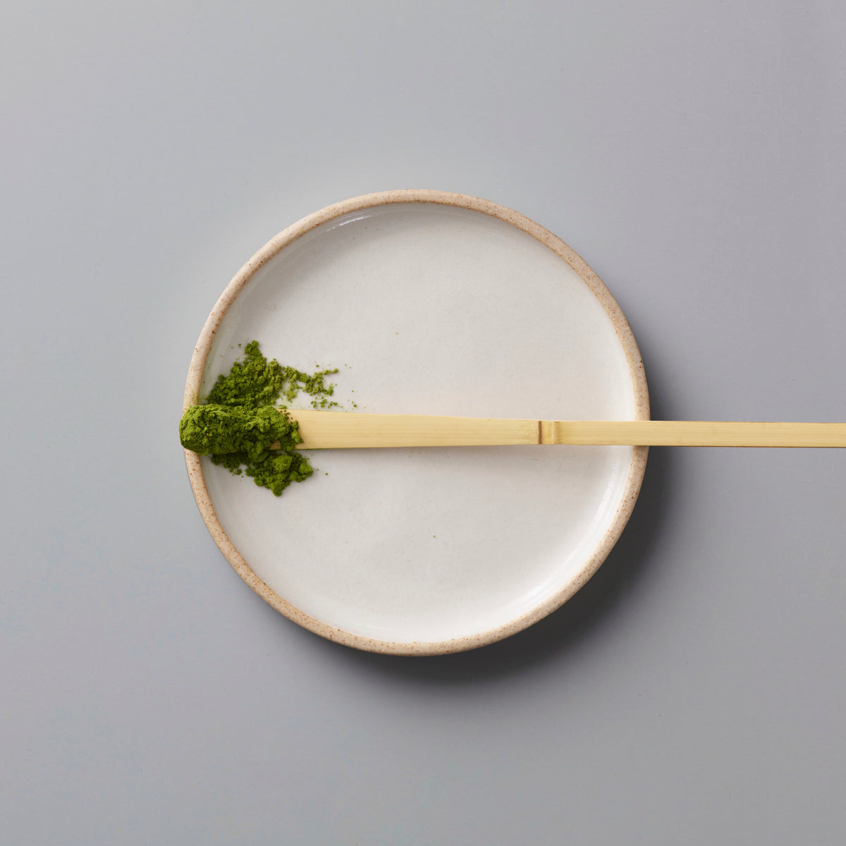 White plate with green powder and a wooden spoon on a gray background