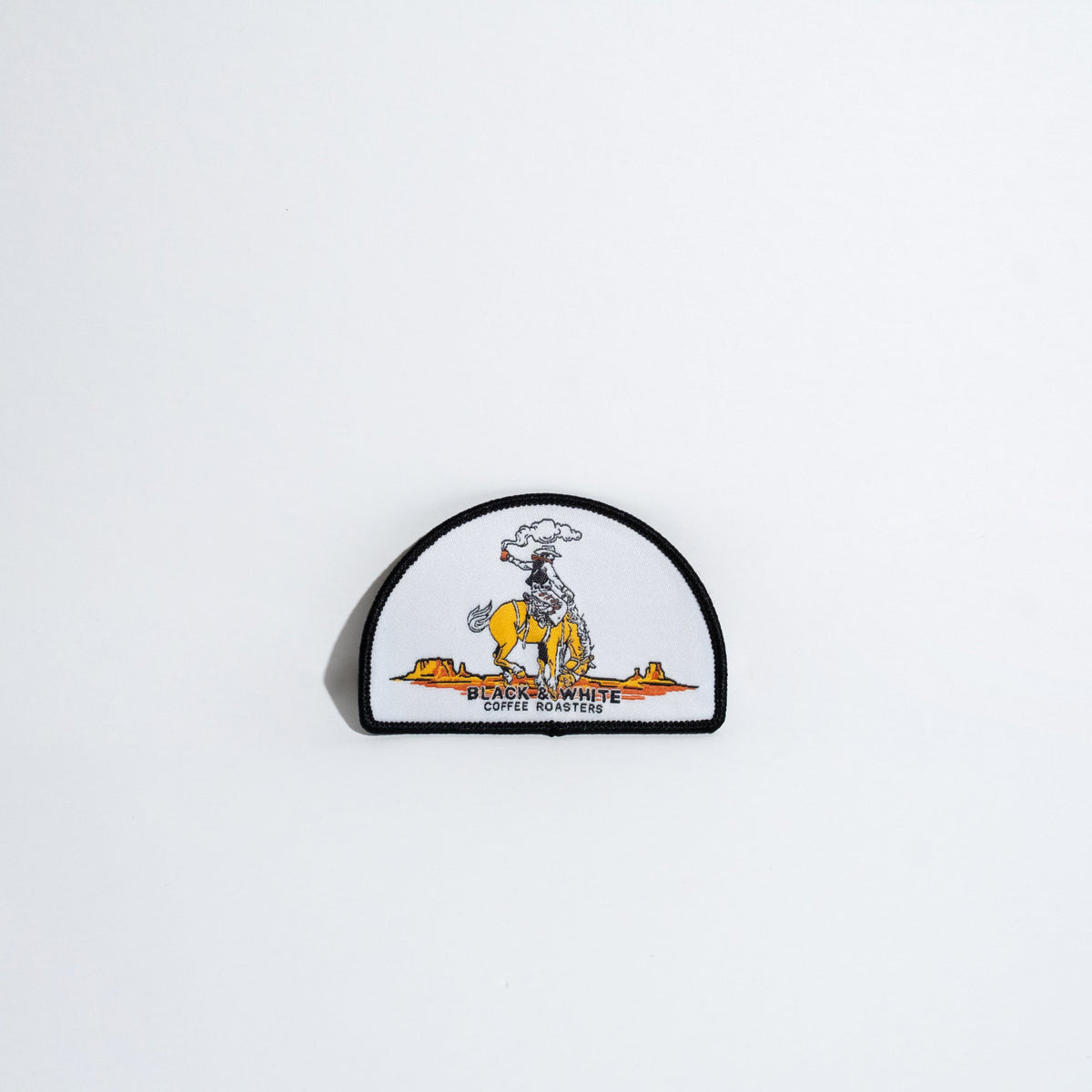 A small embroidered patch featuring a cowboy riding a yellow bucking horse, with the text 'BLACK & WHITE COFFEE ROASTERS' below, shown against a plain white background.