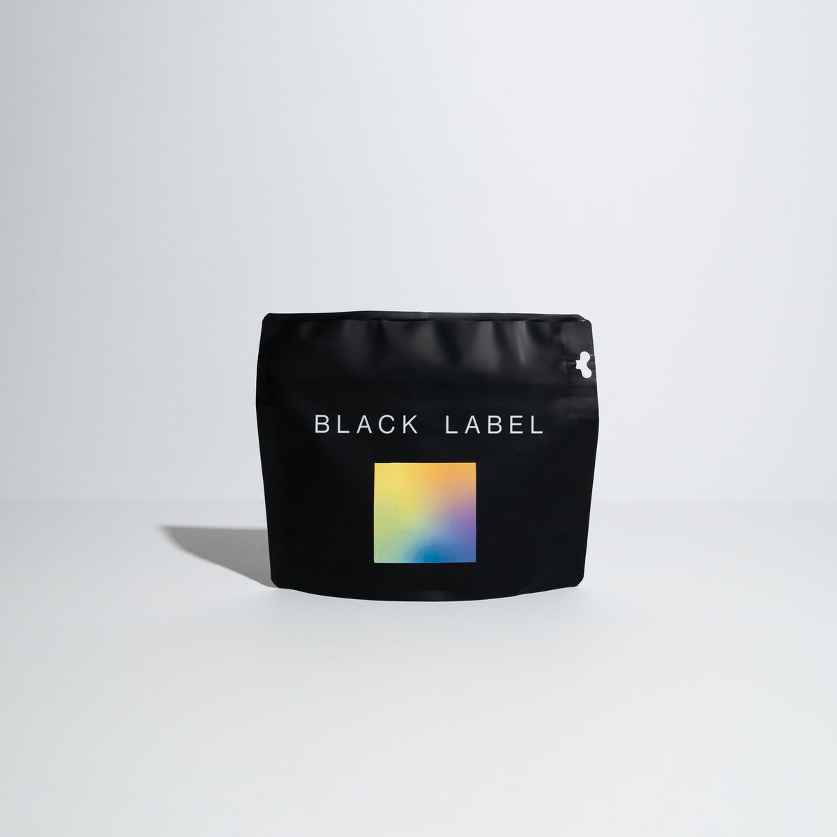 A black bag with the words "Black Label" written in a sans serif modern font covering around 75% of the top portion of the bag. In the center of the black bag is a square label with a morpheus gradient with the colors of light yellow to tangerine orange to a lime green and blue purple. 