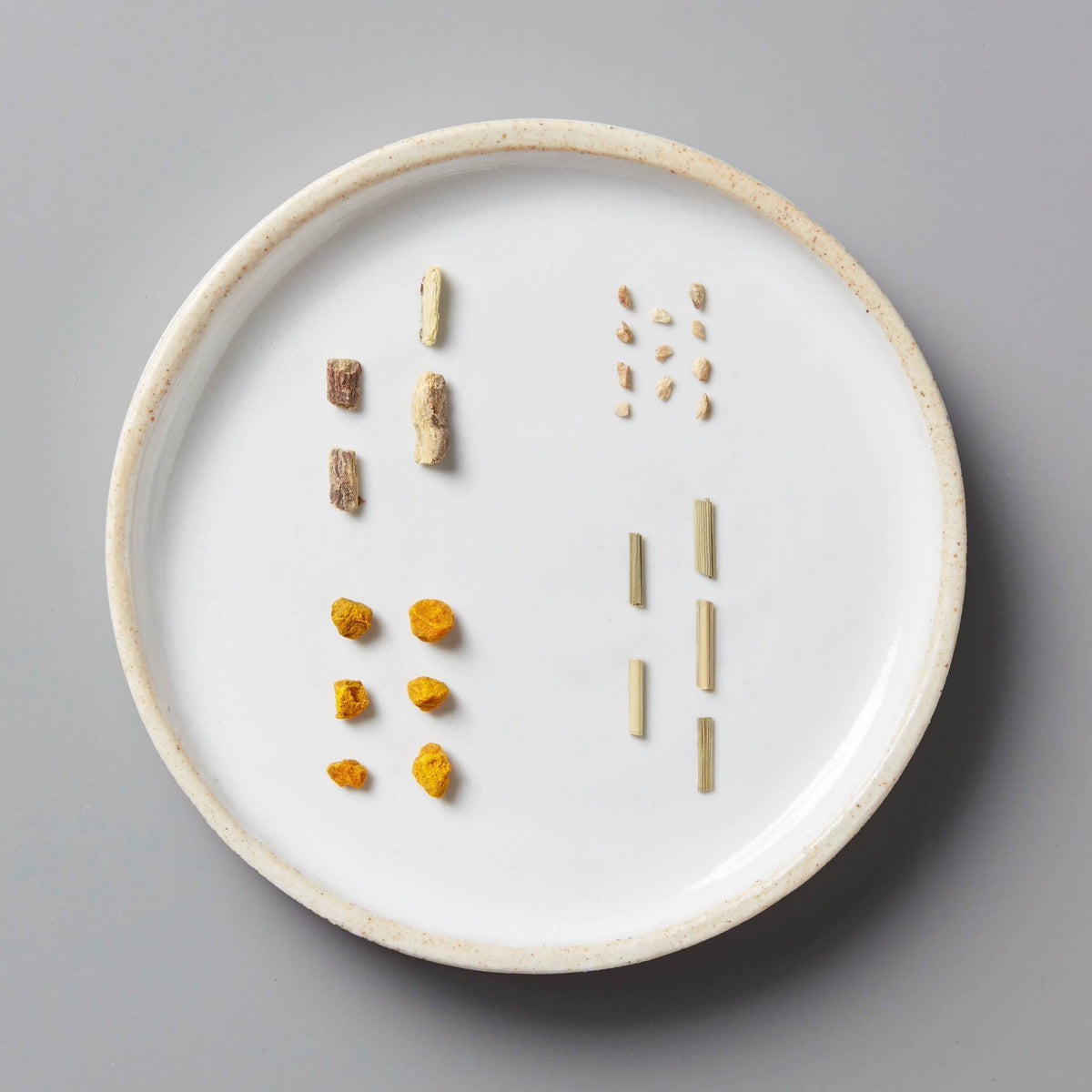 Gold | Tisane Blend: Overhead view of a white plate displaying neatly arranged dried turmeric, ginger, licorice roots, and lemongrass, showcasing a herbal tisane sampler.